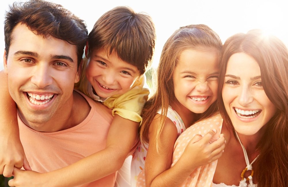 Parents,Giving,Children,Piggyback,Ride,In,Garden